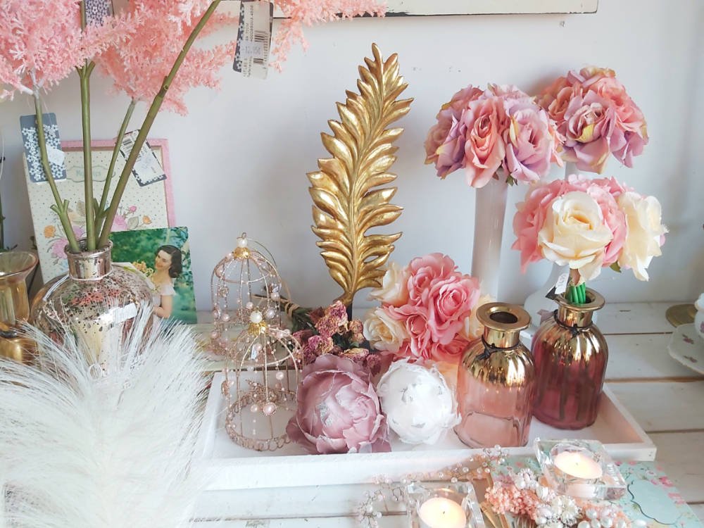 Decoración inspirada en Sentido y Sensibilidad de Jane Austen, floreros, jaulitas y flores de imitación hiperrealistas en tonos suaves, crema y rosa.