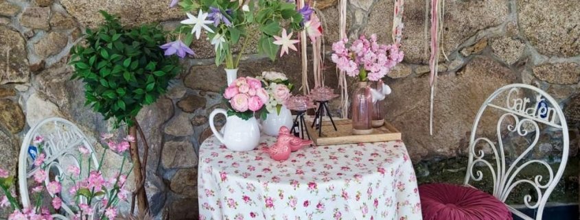 Decoración jardín interior con árboles, plantas y flores artificiales, portavelas de vidrio rosado, lecheras con flores y atrapa-sueños hechos de a mano con materiales naturales