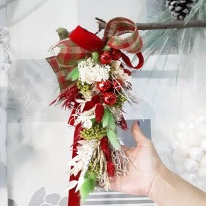 Elaborado en nuestra floristería creativa, te proponemos decoración de Navidad para colgar por su practicidad para decorar puertas, ventanas, paredes. En este caso lleva flores naturales en los colores clásicos de la navidad, verdes, rojos y blancos.s