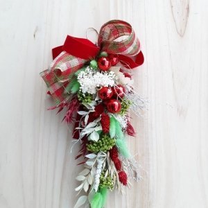 La decoración navideña para colgar es una tendencia en el hogar. En este caso combina flores naturales secas con bolitas de cristal rojas y lazos de cuadros navideños.