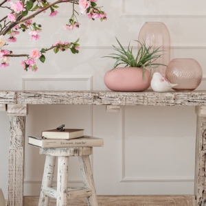 Jarrón decorativo moderno en mesa de madera rústica con detalles decorativos en tonos rosas y blancos