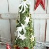 Musgo preservado en árbol navideño para decorar espacios pequeño. Con soporte para sobremesa. Decorado con lazos y bolitas rojas navideñas, estrellas y palomas de madera blanca y guirnalda dorada de estrellas.
